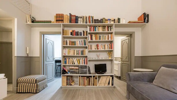 A living room with a grey sofa, a bookshelf filled with books, a television, and a small table.
