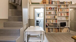 A staircase leading to a landing with a table and chairs, a bookshelf filled with books, and a kitchen area.
