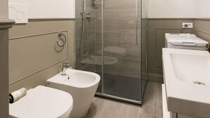 A modern bathroom with a glass-enclosed shower, two bidets, and a sink.