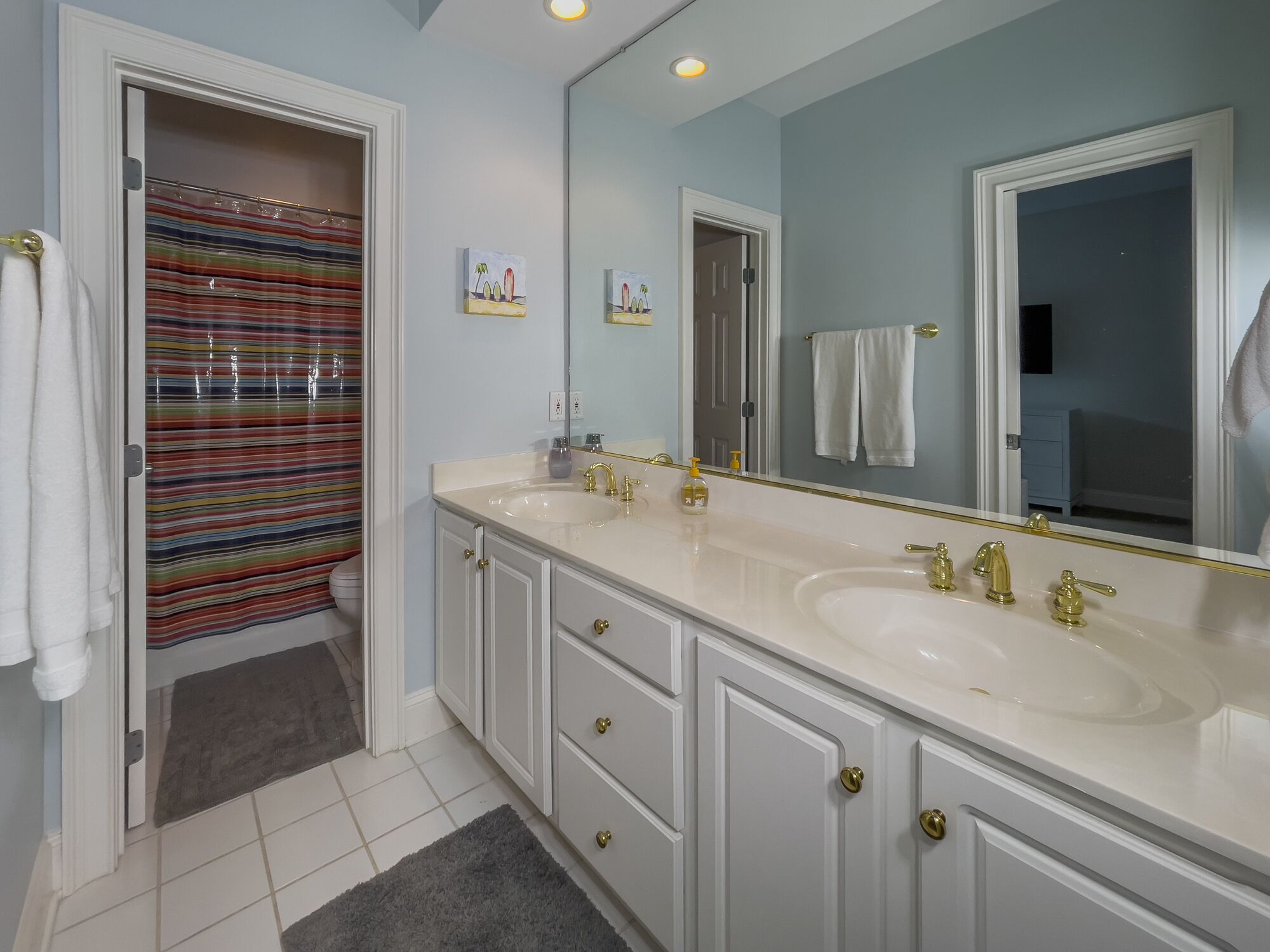 A bathroom with two sinks, a large mirror, and a striped shower curtain.