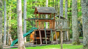 A wooden play structure with a slide and climbing area, surrounded by trees. - Penny Creek Cabin 2 bed 1 bath sleeps 6,Creekside*Hike*Fish*RELAX (Deep Gap)