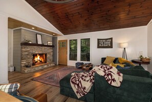 A cozy living room with a stone fireplace, a green sofa, a patterned rug, and a 'These are the good old days' sign.