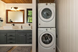 A laundry room with two stacked washing machines, a sink, and a mirror.