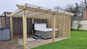 A wooden pergola structure with a hot tub and a storage unit in a backyard. - Daisy Tree Cottage (Woodhall Spa)