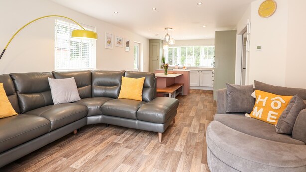 A modern living room with a sectional sofa, a grey armchair, and a wooden herringbone floor. - Daisy Tree Cottage (Woodhall Spa)