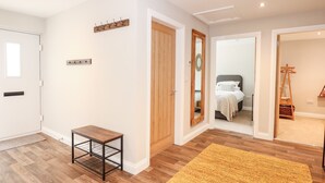 A modern room with wooden flooring, a small table, a mirror, and a bed with a headboard. - Daisy Tree Cottage (Woodhall Spa)