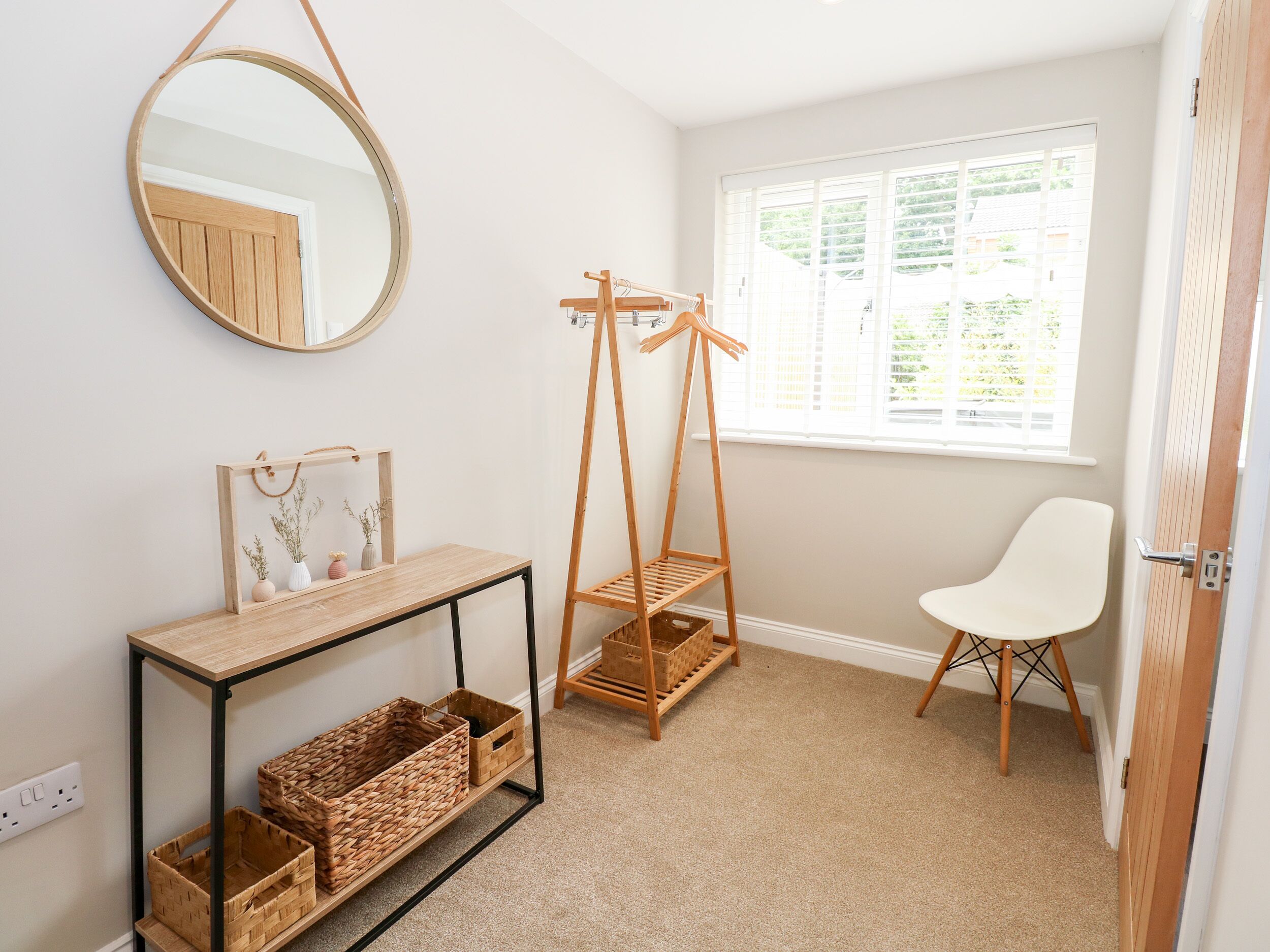 A child's room with a wooden swing, a white chair, a mirror, and a console table with baskets.