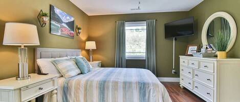 A bedroom with a bed, bedside tables, a dresser, a ceiling fan, a TV, and a window with curtains.