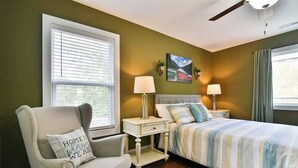 A bedroom with a bed, a chair, a nightstand, and a window with blinds.
