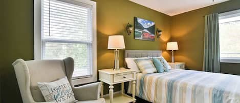 A bedroom with a bed, a chair, a nightstand, and a window with blinds.
