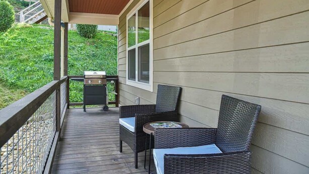 A covered porch with wicker furniture and a small table, overlooking a green landscape.