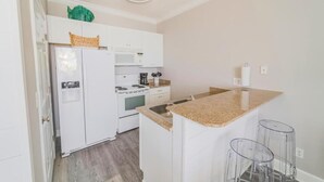 Una cocina compacta con armarios blancos, microondas integrado, estufa y encimera de granito.