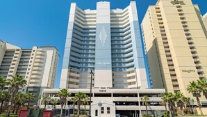 Un hotel de varios pisos con un letrero vertical central, múltiples balcones y un estacionamiento en la parte inferior.