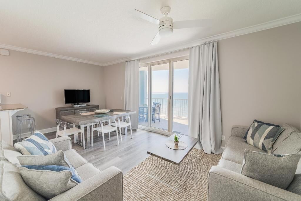 Un salon moderne comprenant un coin repas, un téléviseur à écran plat et un balcon agrémenté de rideaux.