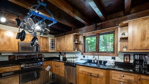 A kitchen with wooden cabinets, a black countertop, a stove, a microwave, and hanging pots.