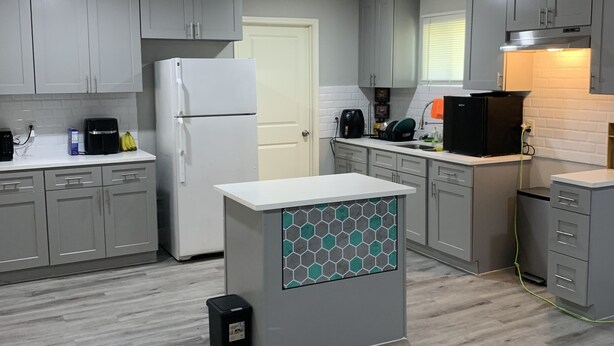 A modern kitchen with grey cabinets, a white refrigerator, a coffee maker, and a microwave. - STOP INN STAY HOSTELS (Houston)