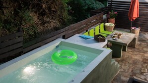A hot tub with a green inflatable ring, surrounded by stone flooring and wooden benches. - DandyVillas Tsagkarada | Sweet Green Apple | Mini Pool (Tsagkarada)