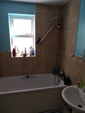 A bathroom with a bathtub, a window, and a shower.