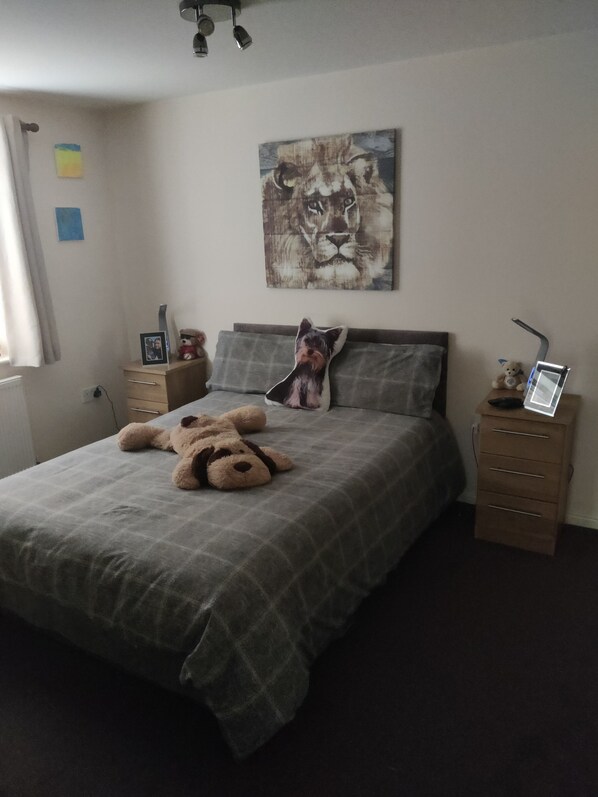 A bedroom with a bed, a teddy bear, a pillow, a nightstand, a lamp, and a painting of a lion.