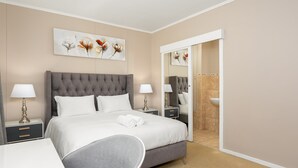 A modern hotel room with a large bed, bedside tables with lamps, a grey armchair, and a bathroom visible through an open door. - Island Club 206 (Cape Town)