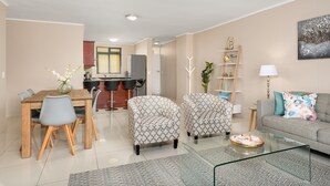 A modern living room with a dining area, a grey sofa, a glass coffee table, and a kitchen in the background. - Island Club 206 (Cape Town)