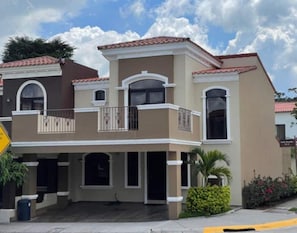 A two-story residential building with a balcony, a garage, and a small garden area.