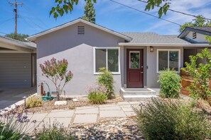 A single-story house with a front porch, a garage, and a small garden with various plants and a pathway.