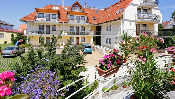 A multi-story residential building with a red-tiled roof, balconies, and a garden with flowers. - Club Unicum Apartman (Hévíz)