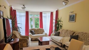 A living room with a sofa, armchairs, a coffee table, and a TV. - Club Unicum Apartman (Hévíz)