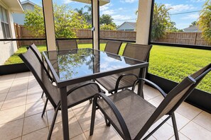 A glass-top table with four chairs, surrounded by a wooden fence and a grassy yard. - Centrally located 4/2 Home with a private backyard available for Longer Stays! (Port St. Lucie)