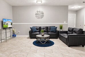 A modern living room with a sectional sofa, a coffee table, and a flat-screen TV on a console table. - Centrally located 4/2 Home with a private backyard available for Longer Stays! (Port St. Lucie)
