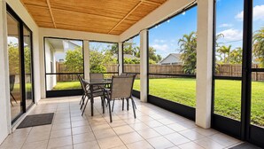 A covered patio with a table and chairs, large windows, and a view of a grassy yard. - Centrally located 4/2 Home with a private backyard available for Longer Stays! (Port St. Lucie)