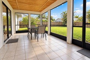 A covered patio with a table and chairs, large windows, and a view of a grassy yard. - Centrally located 4/2 Home with a private backyard available for Longer Stays! (Port St. Lucie)