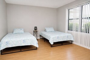 Ein Schlafzimmer mit zwei Betten, einem kleinen Tisch und einem Fenster mit Jalousien.