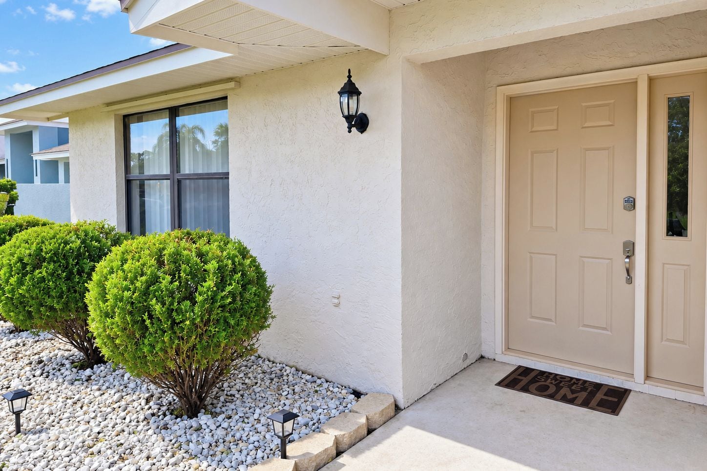 A house with a beige door, a window, and two well-maintained bushes.