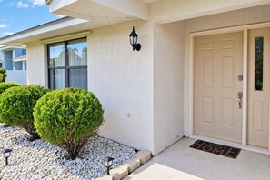 A house with a beige door, a window, and two well-maintained bushes.