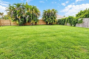 Un jardin avec une clôture en bois, une pelouse verdoyante et des palmiers.