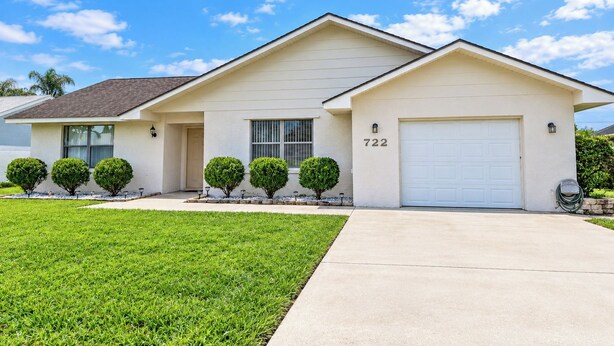 A single-story house with a garage, numbered 722, and a well-maintained lawn. - Centrally located 4/2 Home with a private backyard available for Longer Stays! (Port St. Lucie)