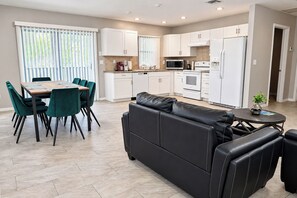 Une cuisine moderne avec des meubles blancs, un coin repas comprenant une table et des chaises, et un canapé en cuir noir.
