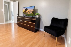 Un salon moderne avec un plancher en bois, un meuble de rangement noir abritant un téléviseur à écran plat, et un fauteuil en velours noir.