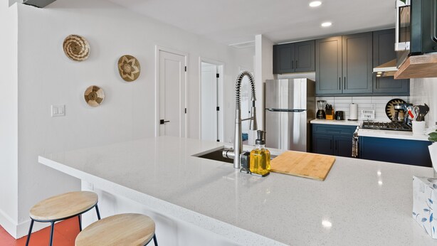 A modern kitchen with a white island, stainless steel appliances, and a blue accent wall. - Newer, Modern, Work Friendly 2 Bedroom Condo near Downtown PHX (Phoenix)