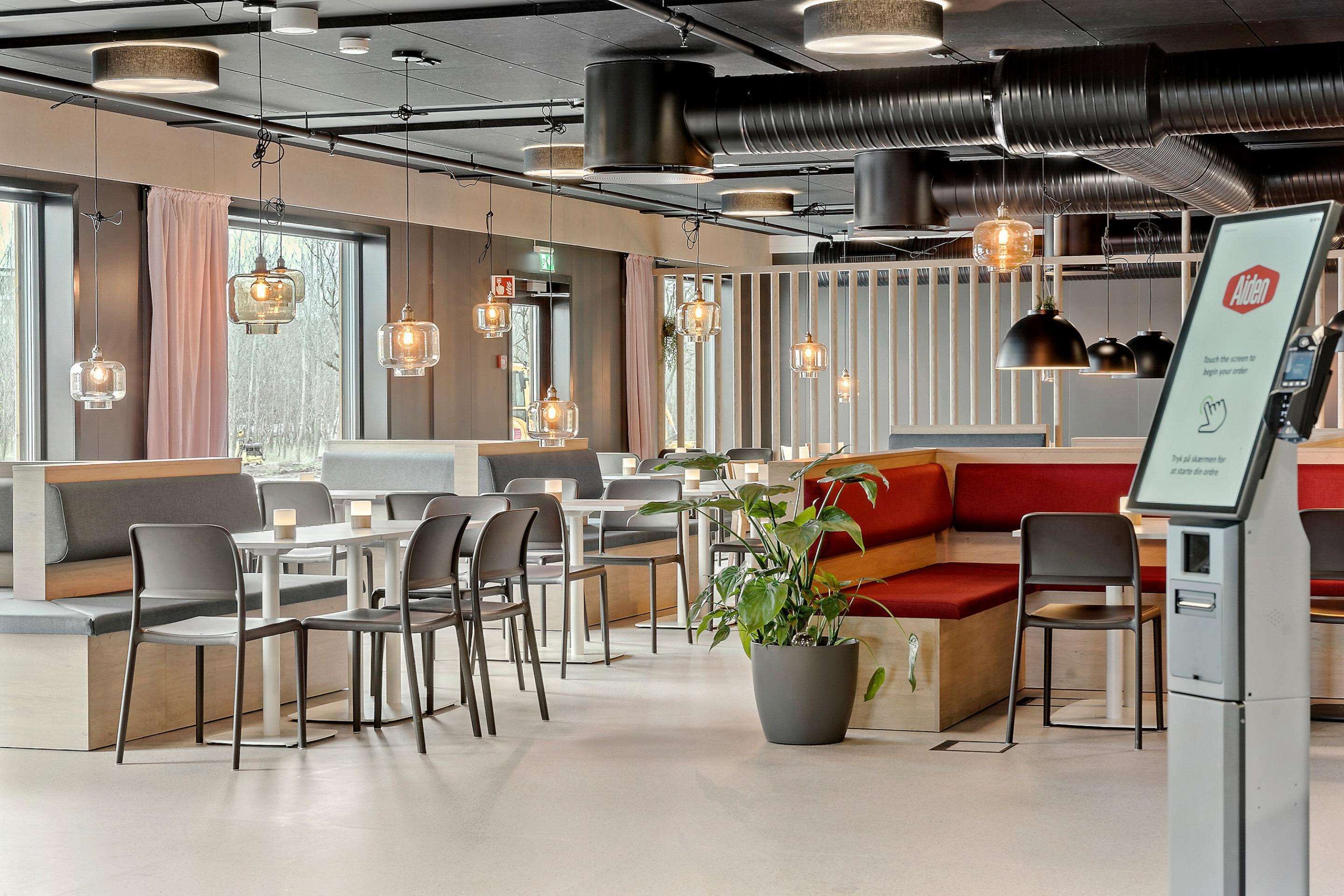 Un restaurante moderno con mesas altas, sillas y una zona de estar con cojines rojos.