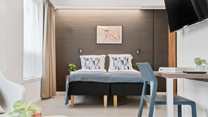 Una habitación de hotel moderna con cama, mesitas de noche, escritorio y televisor.