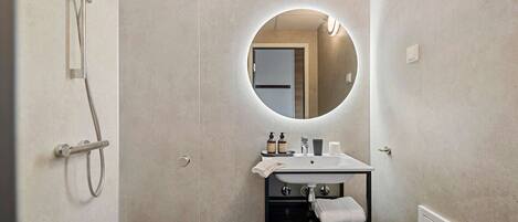 A modern bathroom with a shower, a round mirror, a sink, and a towel rack.