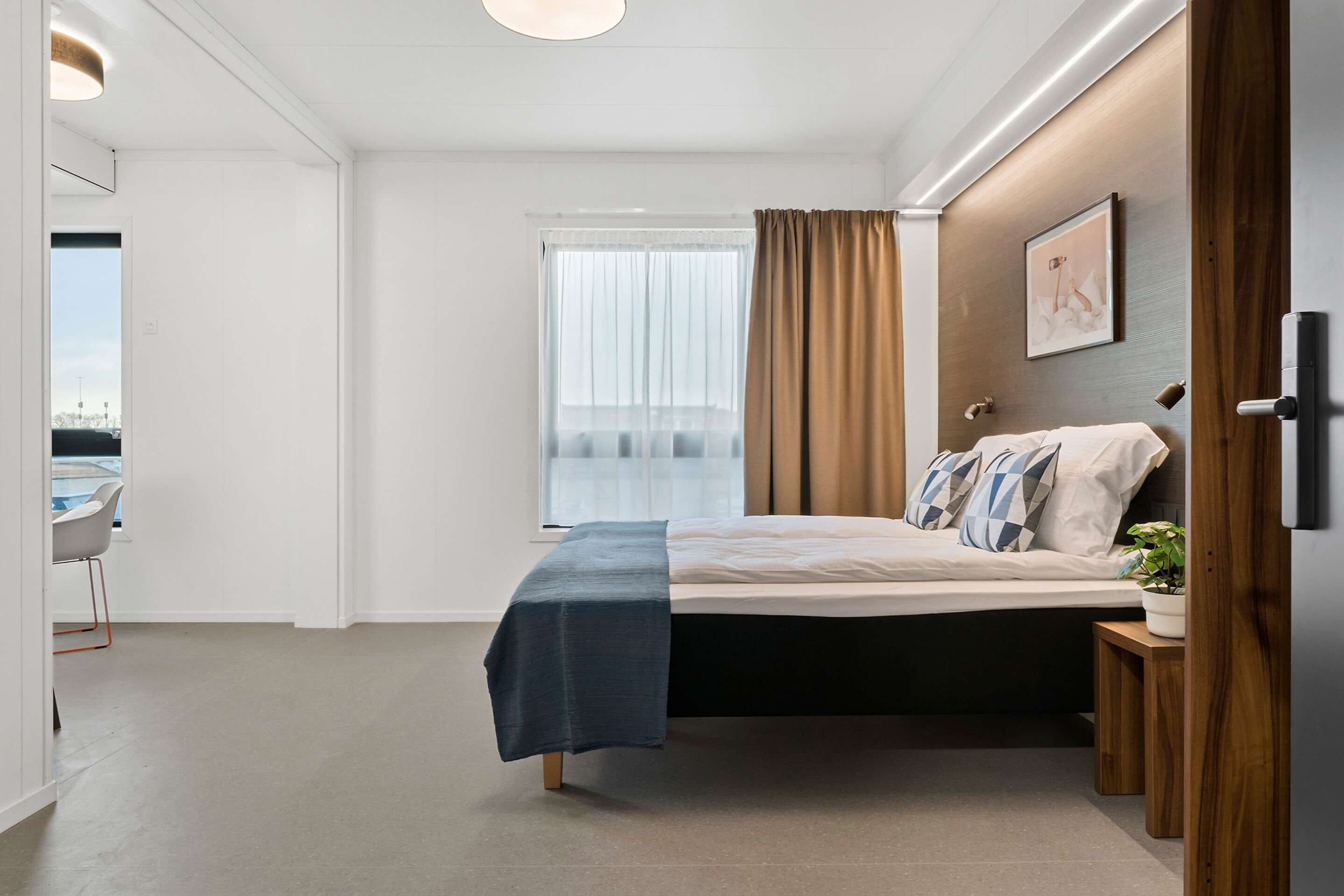 A modern bedroom with a bed, a desk, and a window with curtains.