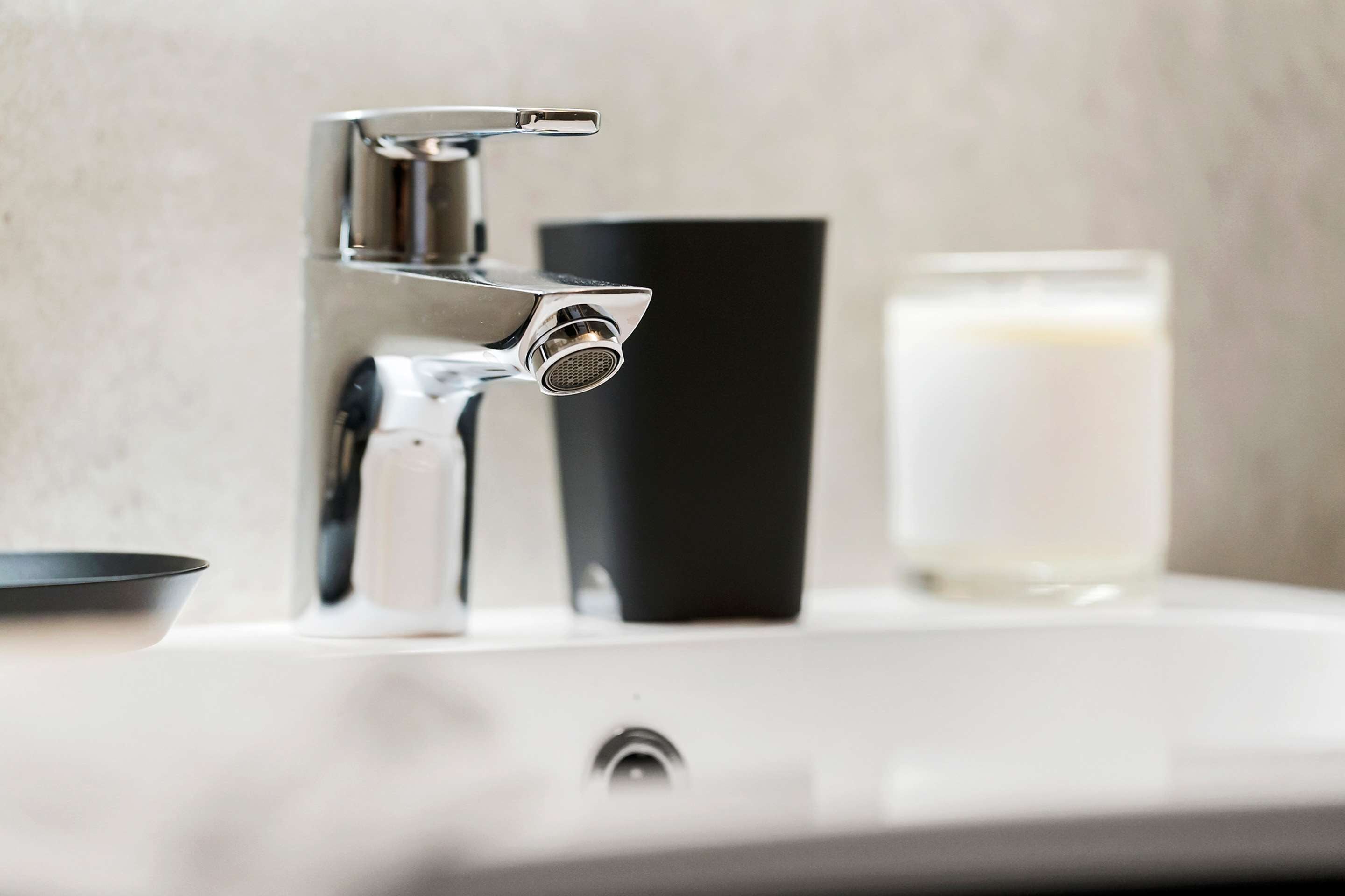 A bathroom sink with a chrome faucet, a black soap dispenser, and a glass of water.