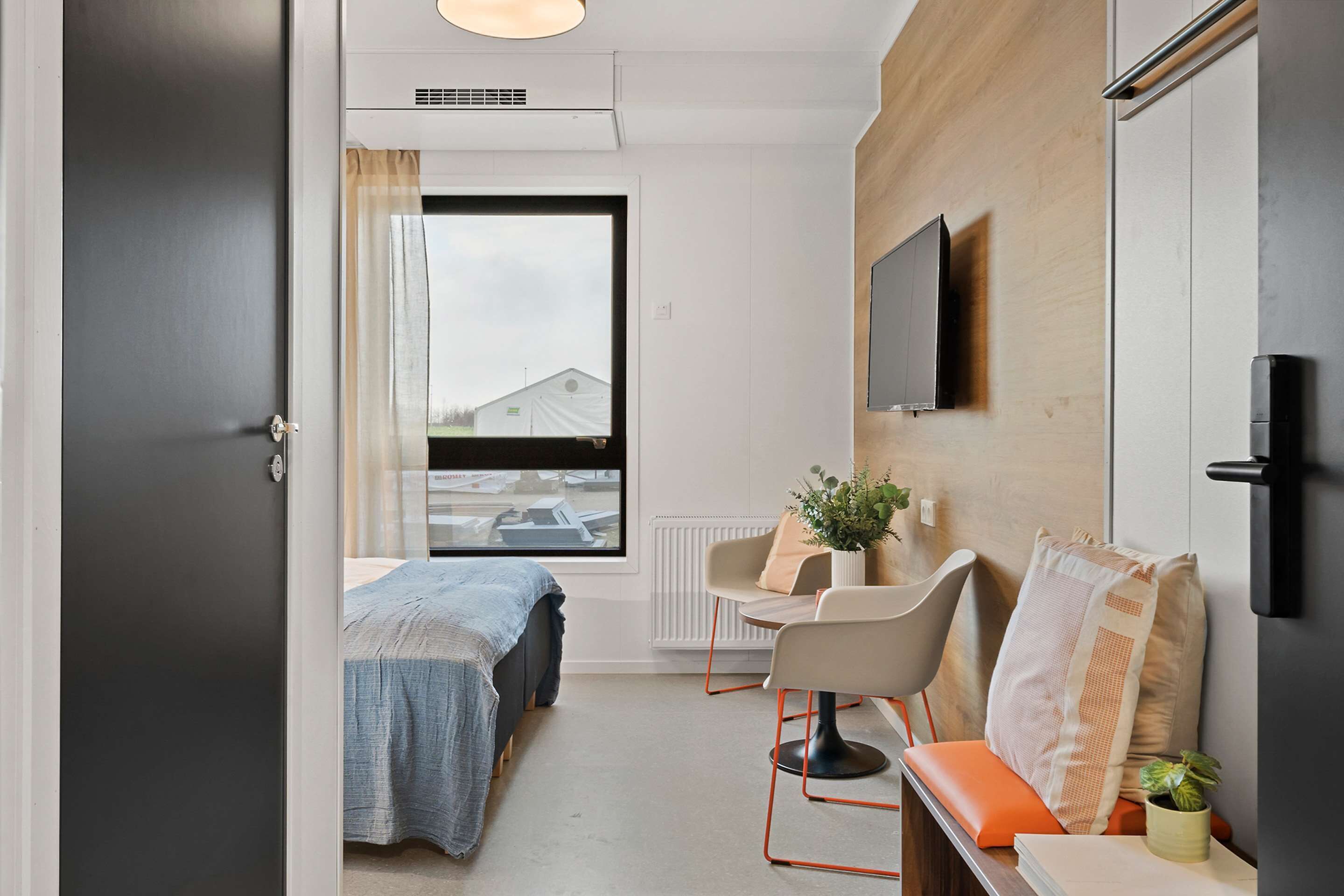 A modern hotel room with a bed, a desk, a chair, and a TV.