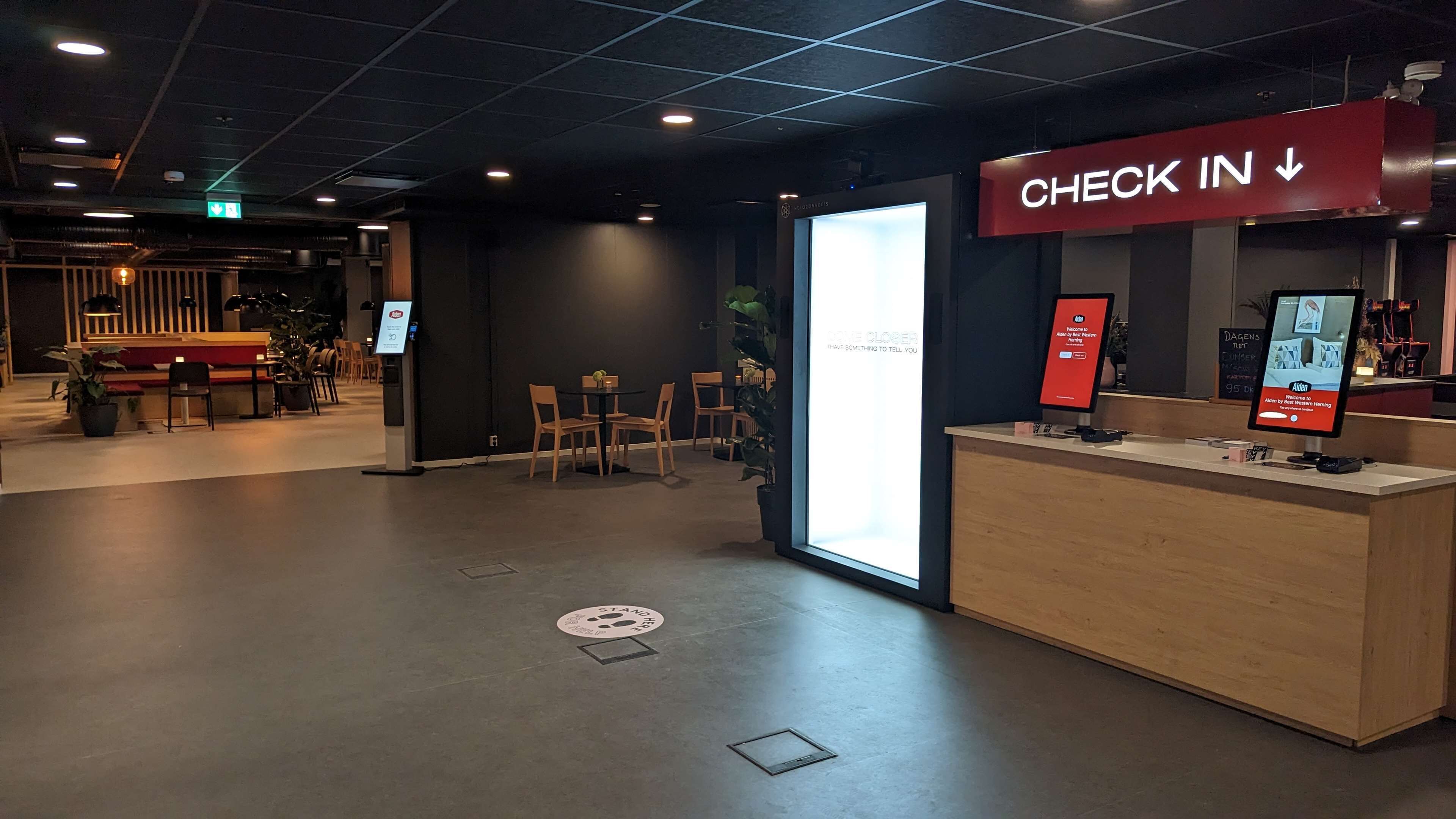 A check-in area with a reception desk, a digital screen, and a sign indicating the check-in direction.