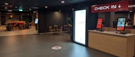 A check-in area with a reception desk, a digital screen, and a sign indicating the check-in direction.