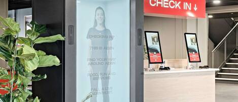 A hotel reception area with a digital screen displaying a welcome message, a 'Check In' sign, and a reception desk with a computer monitor and a tablet.
